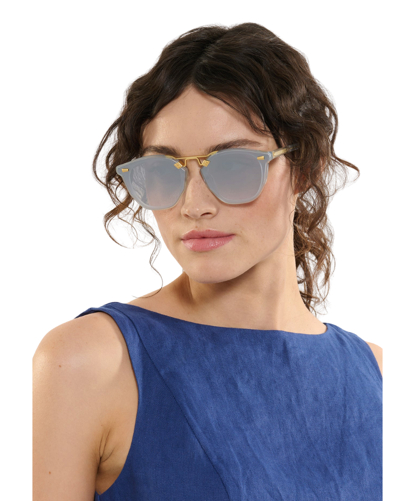 Woman wearing a blue sleeveless top and Krewe sunglasses with a neutral background