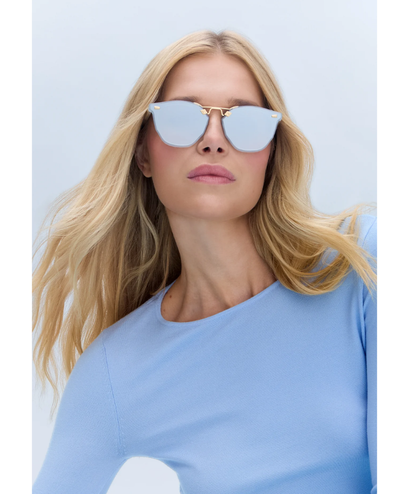 Woman wearing reflective Krewe sunglasses against a light blue background