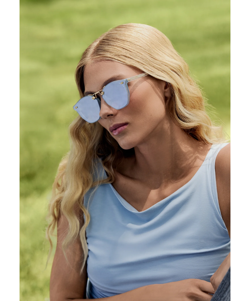 Woman wearing light blue Krewe sunglasses and a matching top outdoors