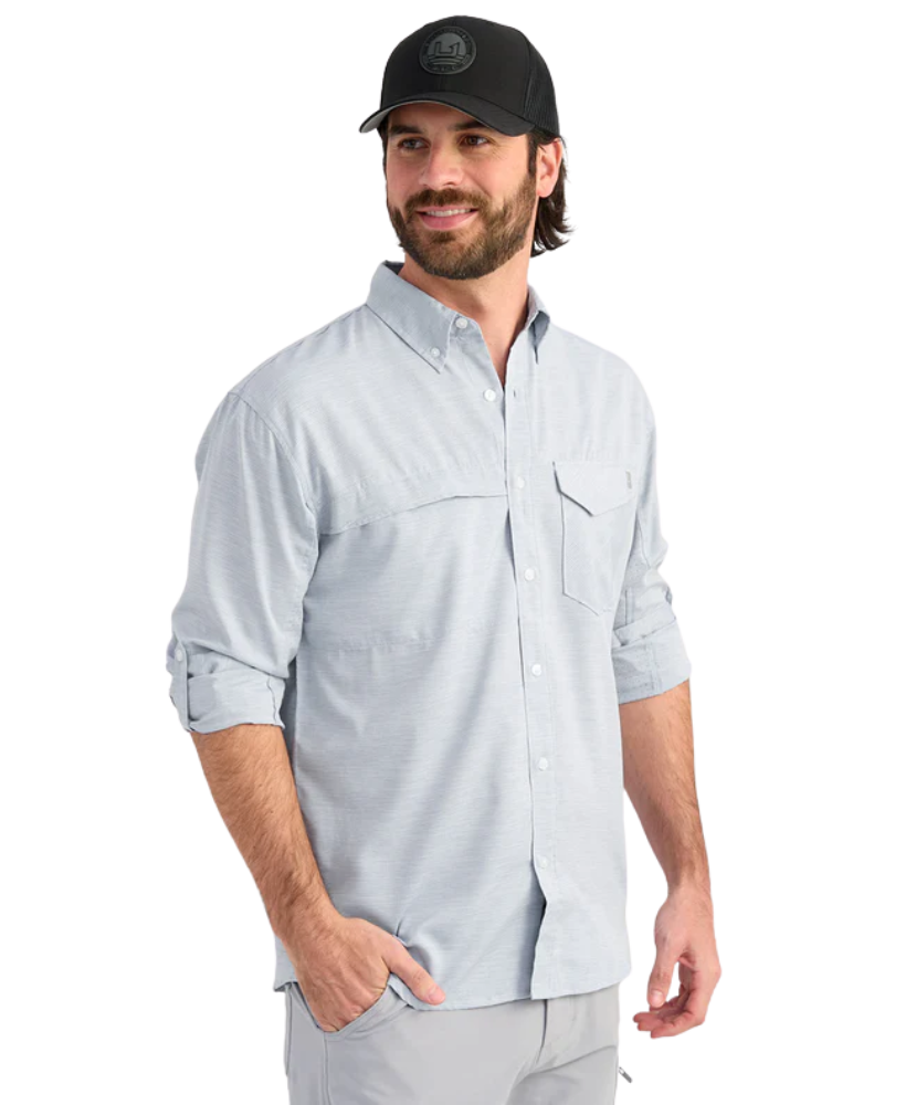 Man wearing a light blue performance HUK button-up shirt and black cap on a white background