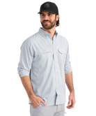 Man wearing a light blue performance HUK button-up shirt and black cap on a white background
