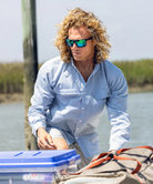 Man wearing a light blue performance HUK button-up shirt and black cap on a white background