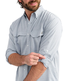 Man wearing a light blue performance HUK button-up shirt and black cap on a white background