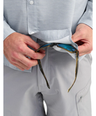 Person wearing a light gray huk button up shirt and pants, cleaning sunglasses with interior glass wipe sunglasses with a white background