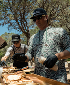 Two men preparing food outdoors, with one wearing a retro duck camoflage hoodie