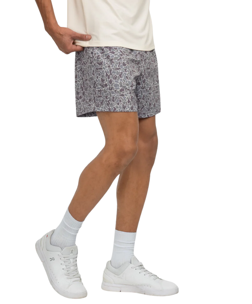 Person wearing a white t-shirt, CAMO patterned shorts, and white sneakers on a white background