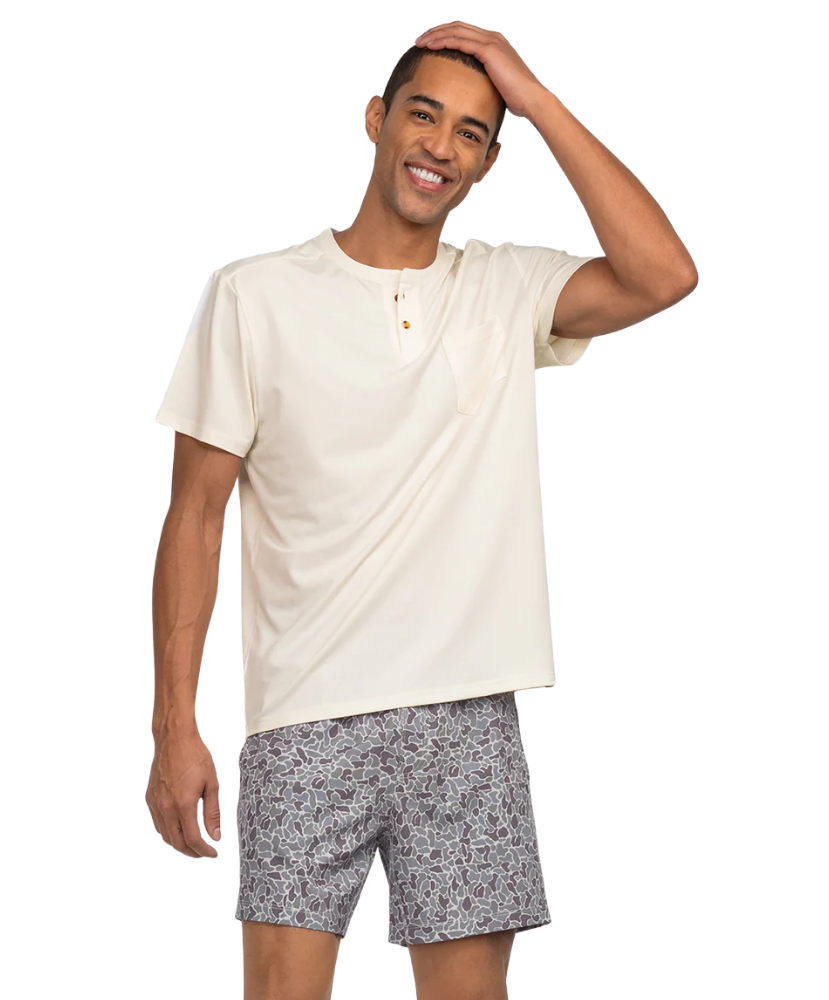 Man wearing a beige shirt and CAMO patterned shorts on a white background