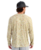 Man wearing a long-sleeve camouflage shirt and cap on a white background