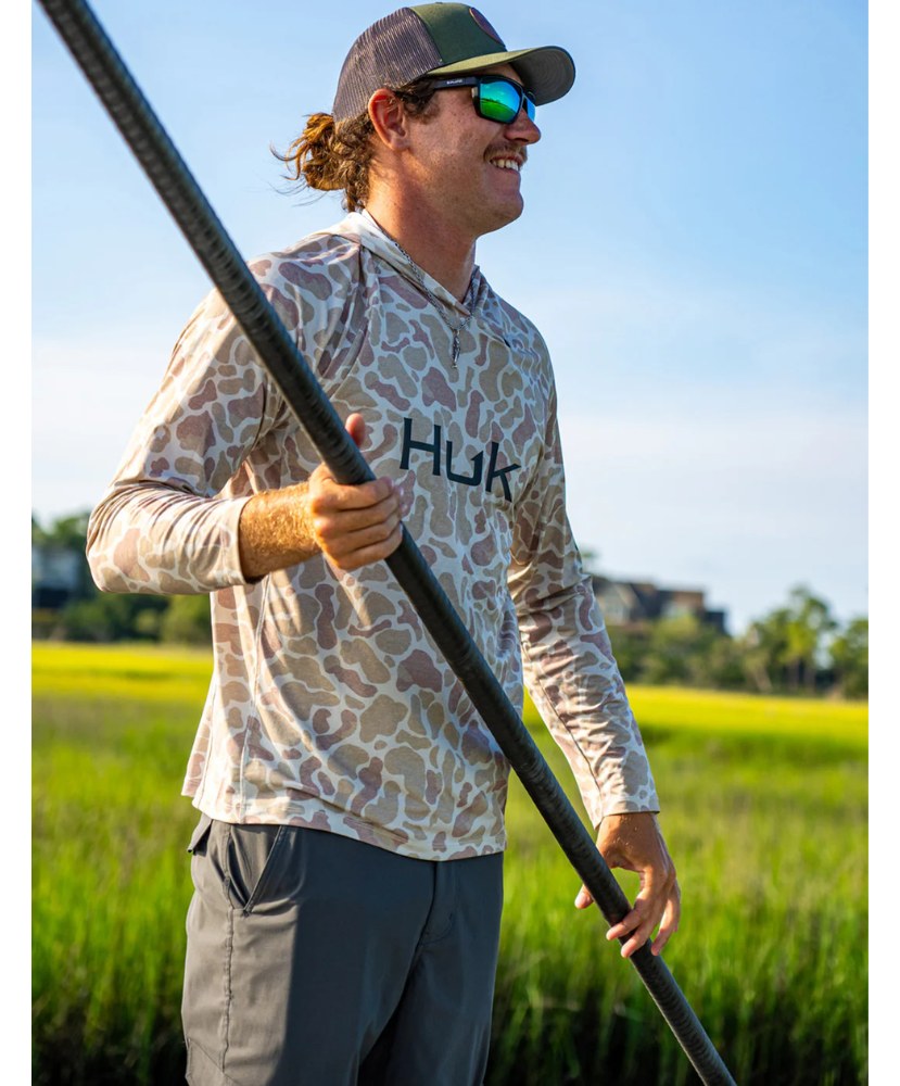 Man wearing a sand camouflage hoodie with 'Huk' branding on a white background