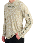 Man wearing a sand camouflage hoodie with 'Huk' branding on a white background
