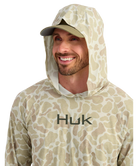 Man wearing a sand camouflage hoodie with 'Huk' branding on a white background