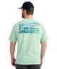 Man wearing a light green HUK t-shirt with a fish lure design and 'Fishing' text, standing against a white background.