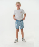 Young boy wearing a white t-shirt and blue camo swim shorts on a white background