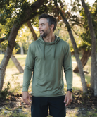 Man wearing a green hoodie standing outdoors with trees in the background