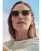Woman wearing Krewe sunglasses with a plain background