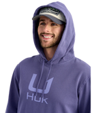 Man wearing a purple hoodie with 'HUK' logo and a cap on a white background