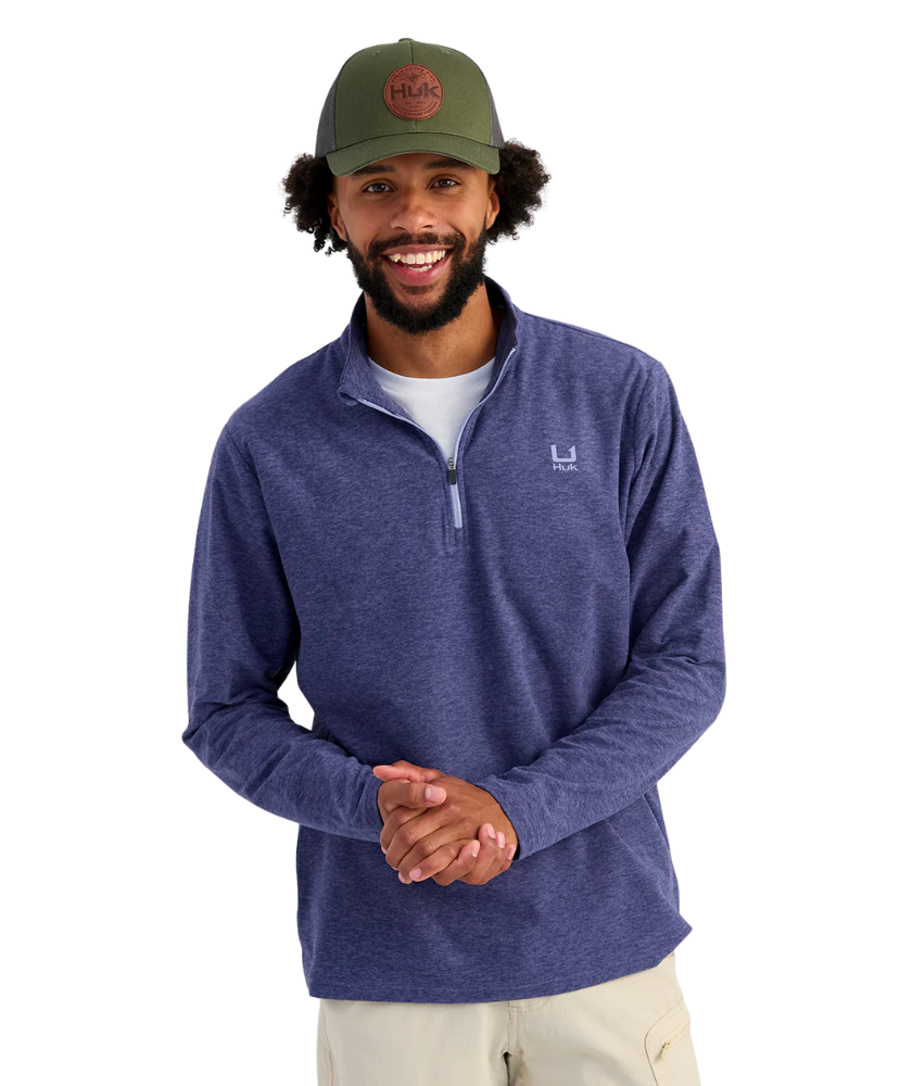 Man wearing a blue pullover with a HUK logo and a green cap with a logo on a white background