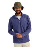 Man wearing a blue pullover with a HUK logo and a green cap with a logo on a white background