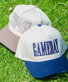 Two hats on grass, one with 'Tailgate Captain' text and the other with 'GAMEDAY' text.
