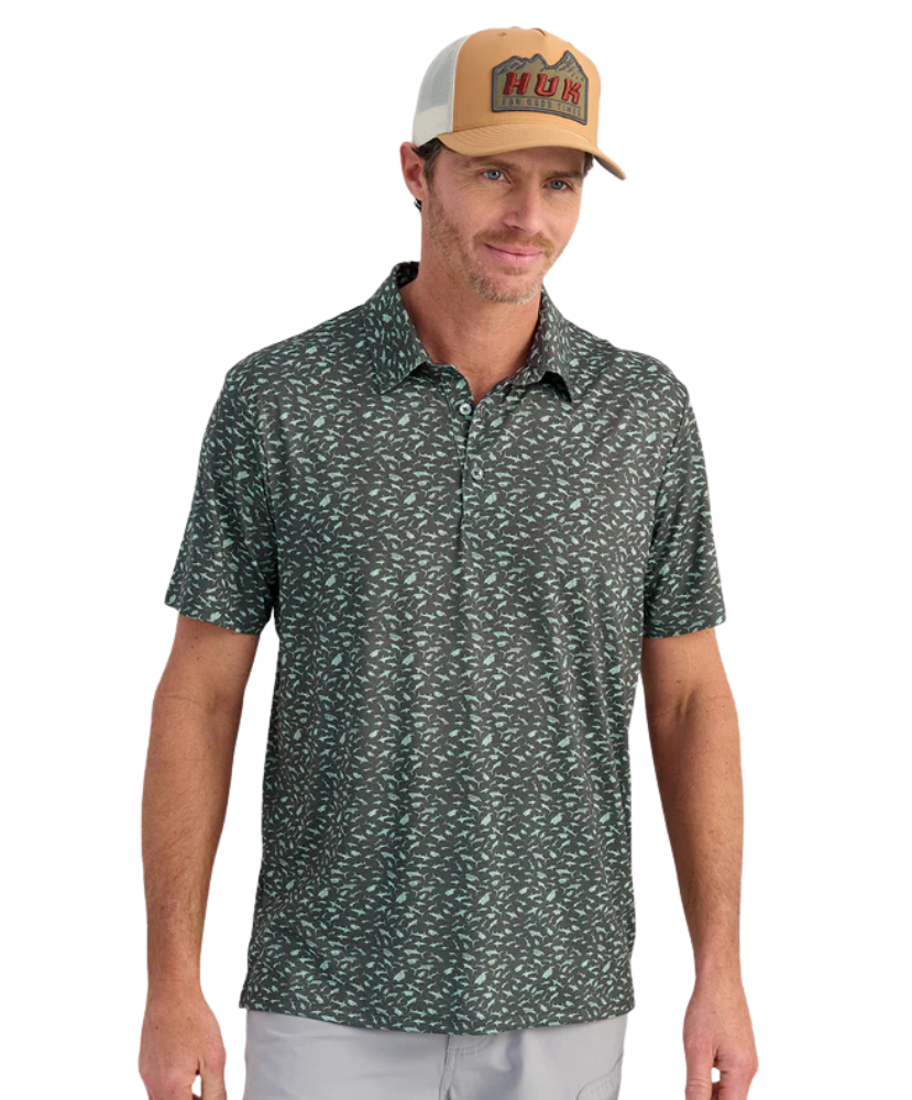 Man wearing a patterned green polo shirt and a tan and brown cap on a white background