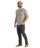 Man wearing a camouflage t-shirt and dark pants on a white background