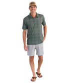 Man wearing a patterned polo shirt and light shorts on a white background