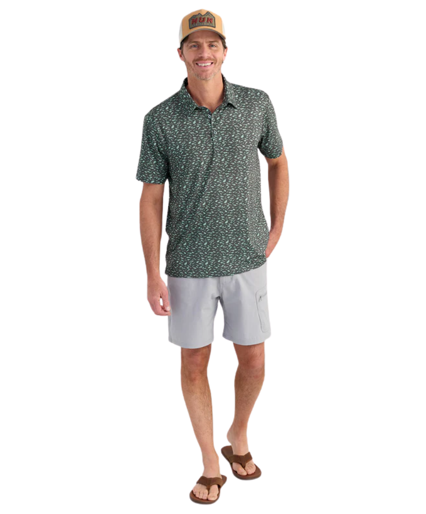 Man wearing a patterned polo shirt and light shorts on a white background