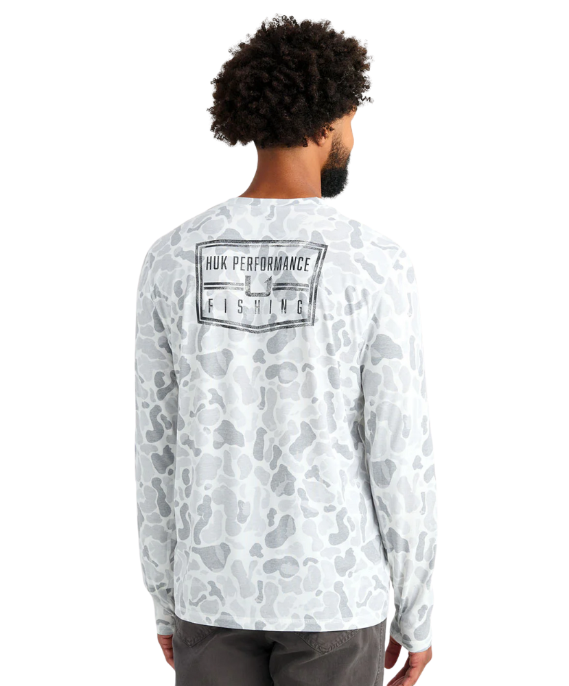 Man wearing a white camouflage long-sleeve shirt with 'Huk Performance Fishing' logo on the back.