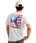 Man wearing a USA HUK white t-shirt with an American flag and marlin tail graphic design on the back, standing against a white background