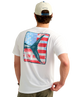 Man wearing a USA HUK white t-shirt with an American flag and marlin tail graphic design on the back, standing against a white background