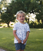 Young boy standing outdoors in a grassy area with trees in the background