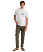 Man wearing a white t-shirt with a HUK logo and green pants on a white background