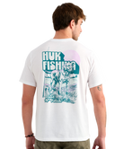 Man wearing a white Huk Fishing t-shirt with a graphic of a dog on the back.