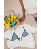 Blue bikini top on a white towel with a bottle of wine and lemons in a basket.