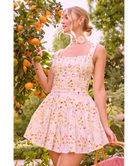 Woman in a floral dress standing in an orchard with orange trees.