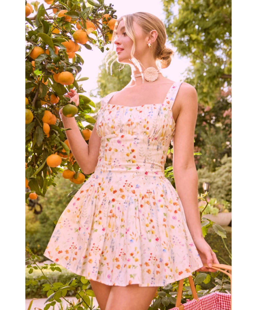 Woman in a floral dress standing in an orchard with orange trees.