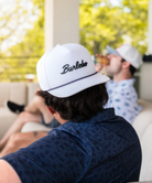 Person wearing a white 'Burlebo' cap sitting outdoors with blurred background