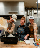 Three people in a kitchen, with one person pouring a liquid into a bowl.