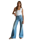 Woman wearing a white tank top and blue flared jeans on a white background