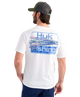 Man wearing a white Huk Fishing t-shirt with a fishing lure graphic on the back, standing against a white background.
