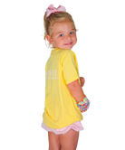 Young girl wearing a yellow shirt with text and pink shorts on a white background