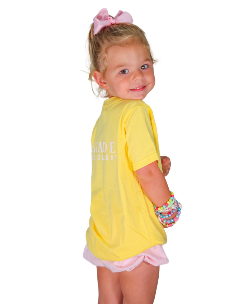 Young girl wearing a yellow shirt with text and pink shorts on a white background