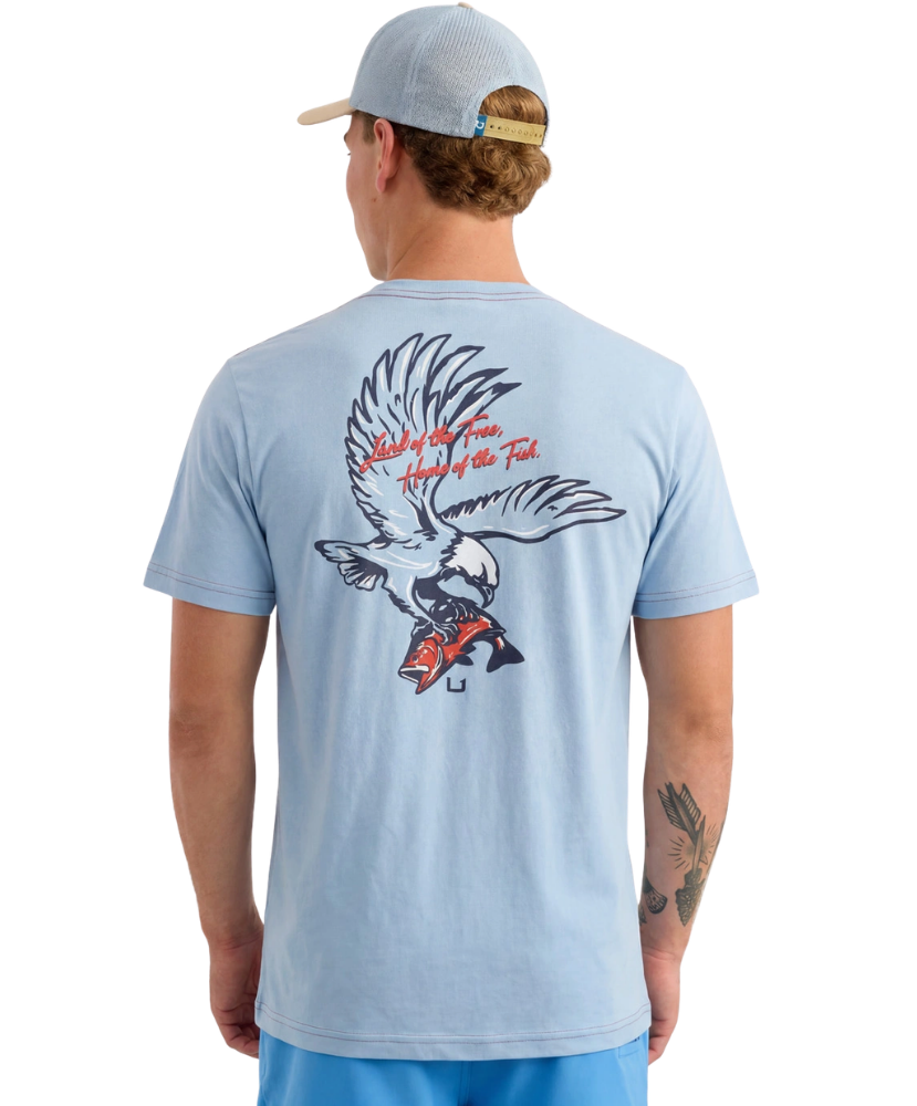 Man wearing a light blue HUK t-shirt with an eagle design on the back, standing against a white background.