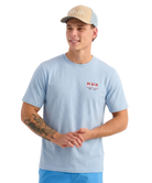 Man wearing a light blue HUK shirt and beige cap on a white background