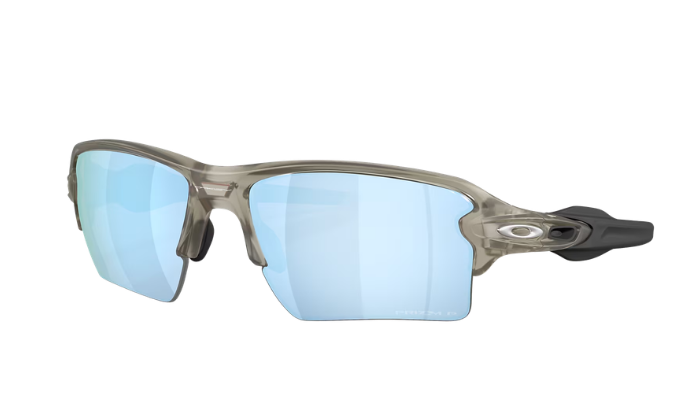 Oakley sunglasses with a translucent smoky gray frame and light blue mirrored lenses, shown from a three-quarters angle on a white background.