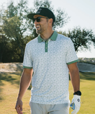 Man wearing a white duck and waterfowl patterned polo shirt with green accents on a white background