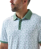 Man wearing a white duck and waterfowl patterned polo shirt with green accents on a white background