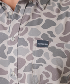 Person wearing a camouflage-patterned button-down shirt with a visible brand logo on a white background