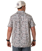 Person wearing a camouflage-patterned button-down shirt with a visible brand logo on a white background