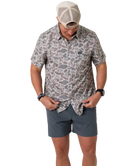 Person wearing a camouflage-patterned button-down shirt with a visible brand logo on a white background